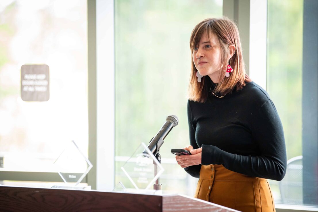 Haylee Shull stands at a podium, reading an excerpt from her piece
